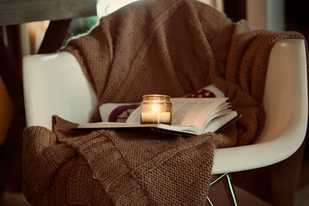 A cozy chair with a book and candle for returning to a relaxed reading habit